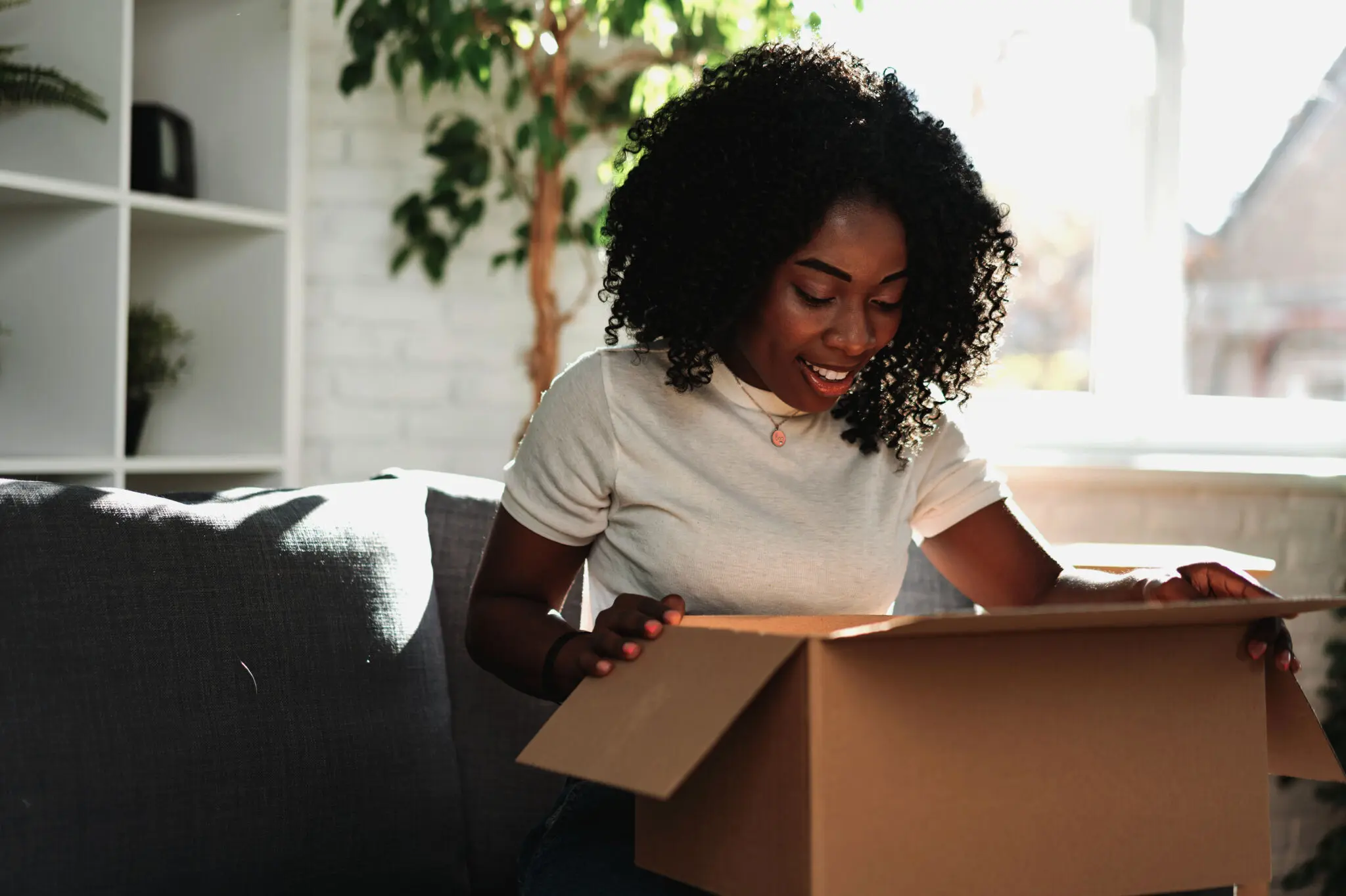 Woman smiling while opening a cardboard delivery box from Landmark Global in a bright living room.