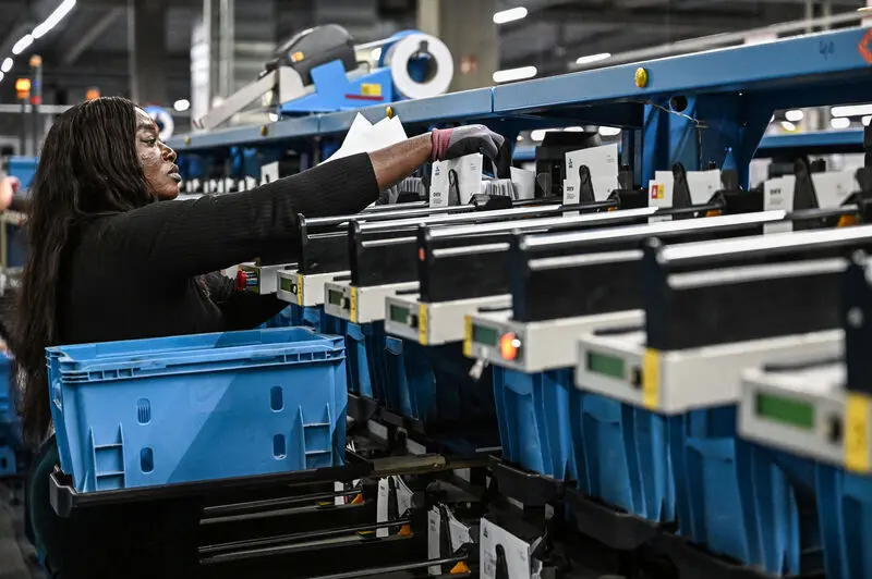 Worker in a black top sorting mail items into blue bins at an automated Landmark Global processing facility.